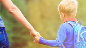 boy wearing backpack holding mother's hand