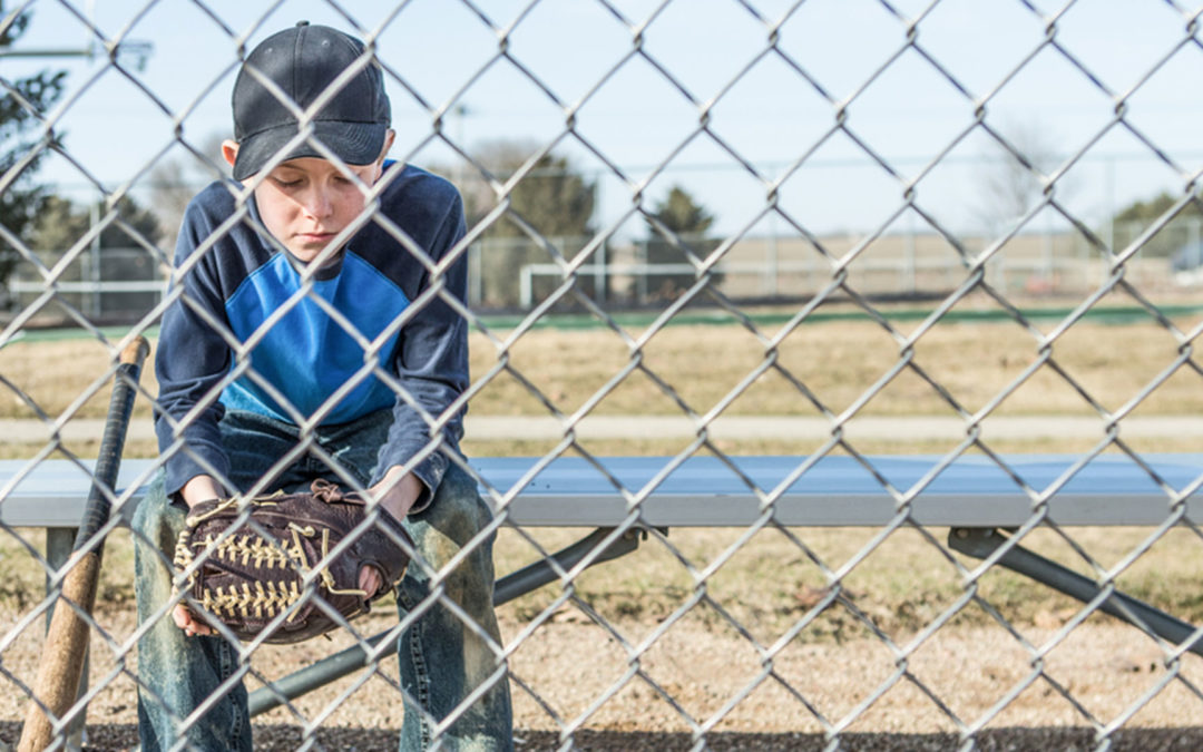 Young baseball player sitting on bench behind fence