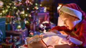 young boy opening gift in front of decorated Christmas tree