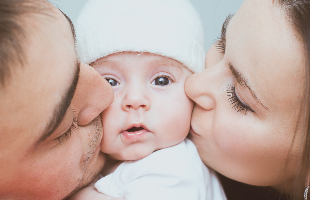Mom and dad kissing newborn baby