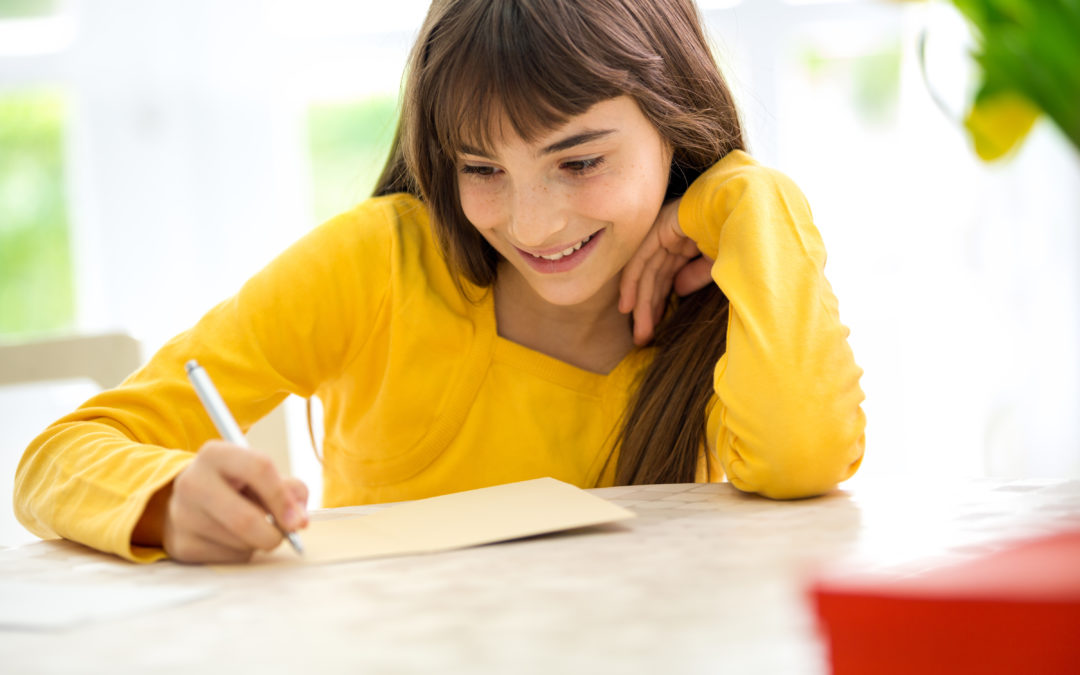 Cute smiling girl writing a letter sitting at desk