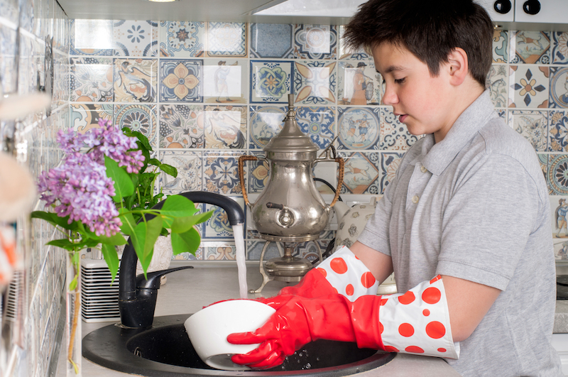 young boy cleaning dishes at home