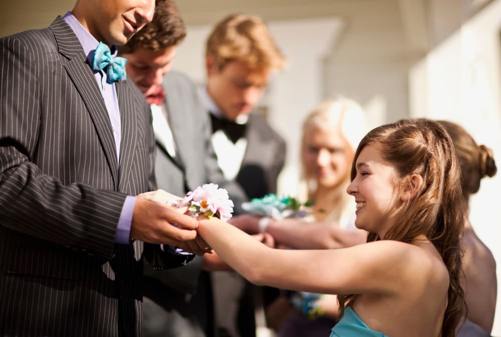 Teenage boys giving their prom dates their corsages.