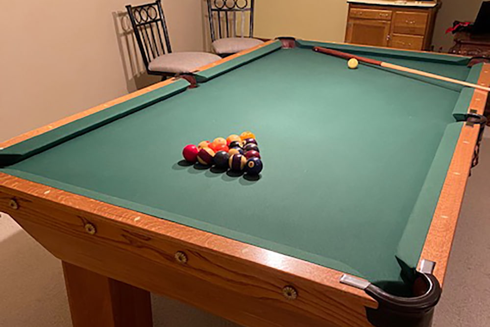 Green carpeted pool table with pool ball triangle, cue ball, and pool stick.