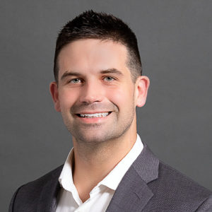 Photo of Nate Christensen headshot wearing gray suit with white undershirt on gray backdrop
