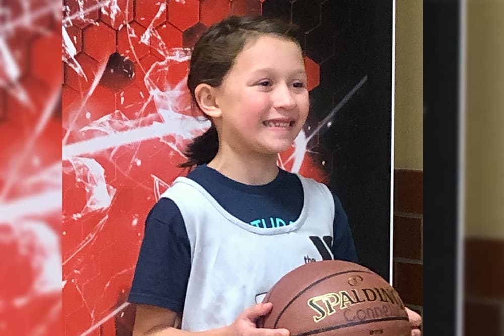 Young girl in YMCA basketball jersey holding basketball in front of red backdrop while getting photo taken