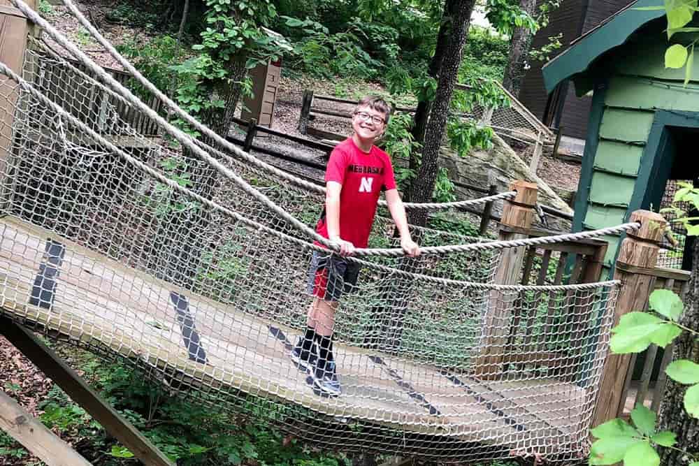 12-year-old boy posing for photo on swinging bridge while holding handrail