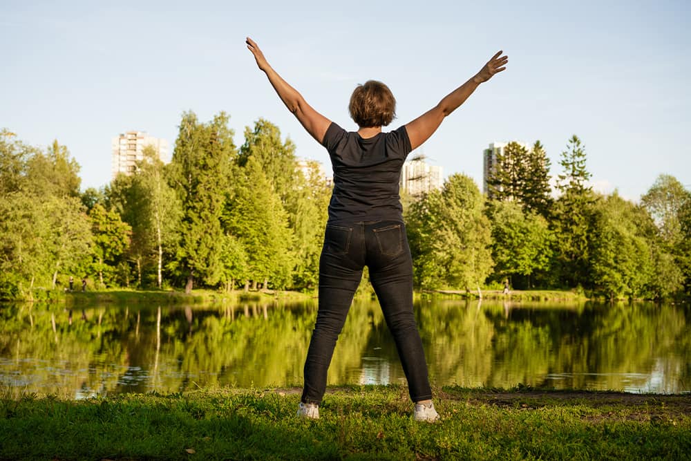 woman with back to camera with outstretched arms looking at lake