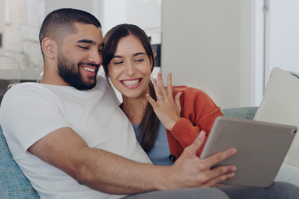 happy engaged couple video calls friends from the couch and shows off the ring