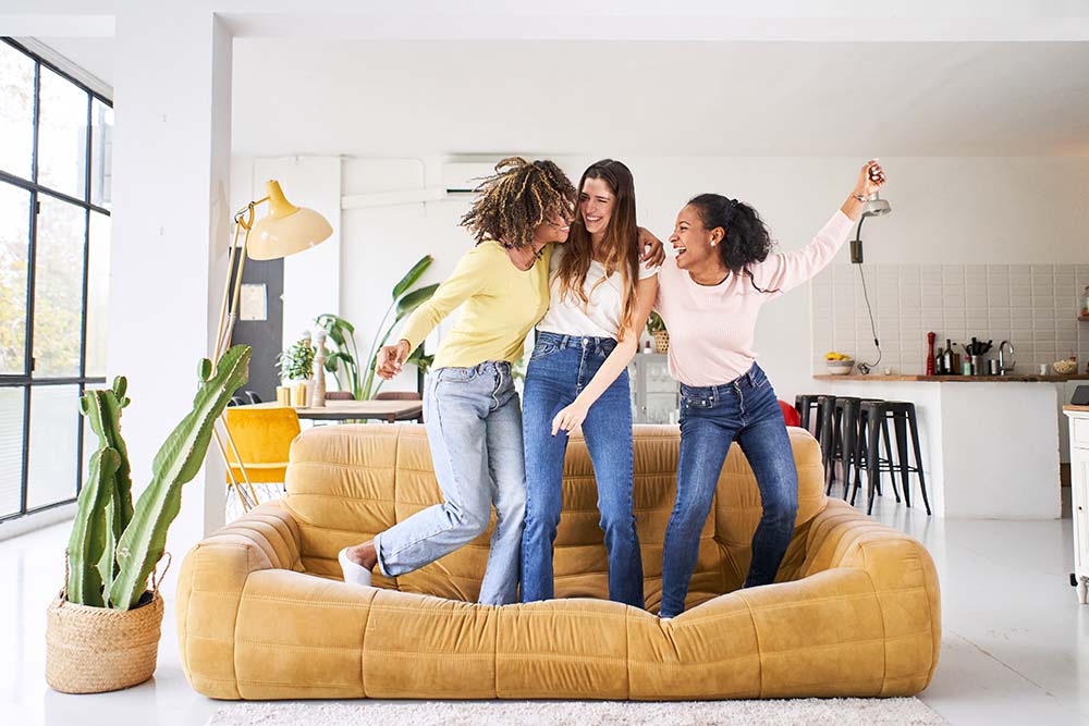 Three young female friends dancing and singing on the sofa at home