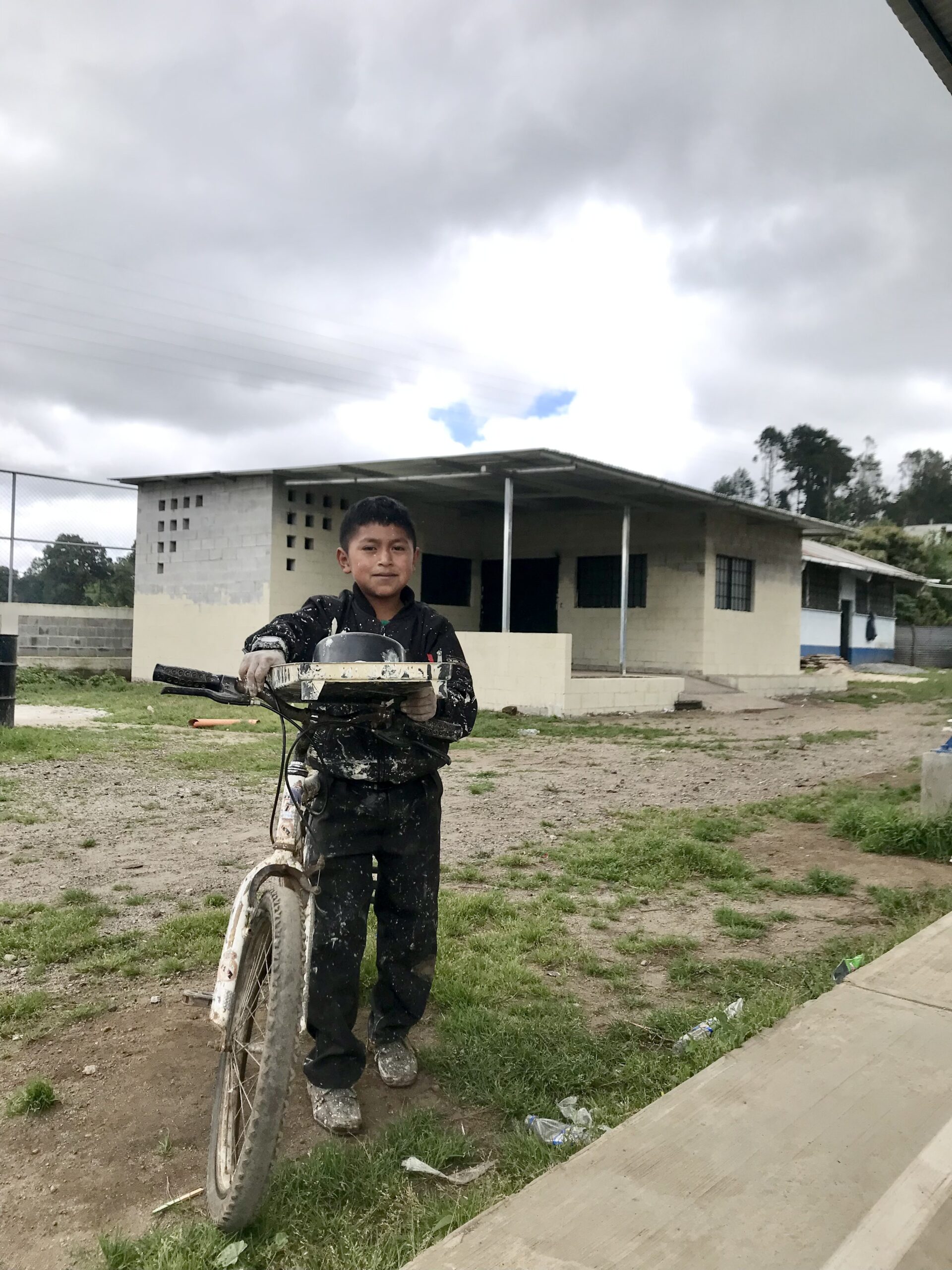 Guatemalan boy with bicycle standing outside newly constructed home
