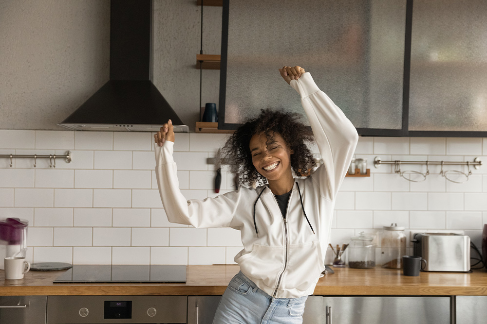woman dancing in kitchen smiling with hands above her head