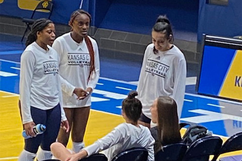 College volleyball players standing at sideline talking to coach sitting on bench