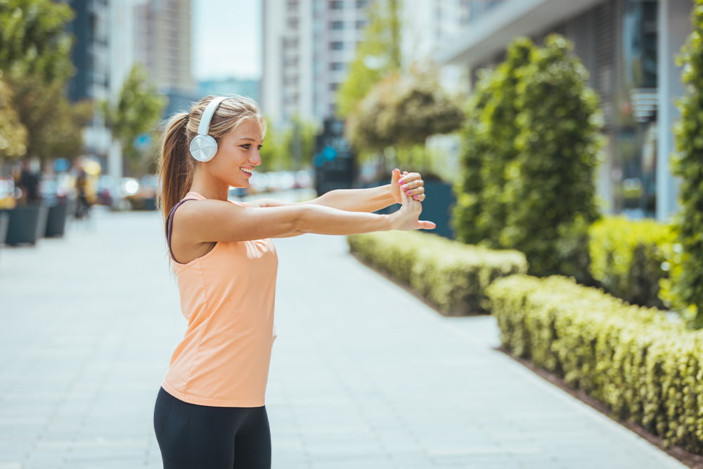 Young athletic woman wearing headphones stretches before a run outside