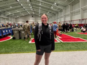 Nancy's granddaughter posing in front of indoor track with hydration backpack before the Lincoln half marathon