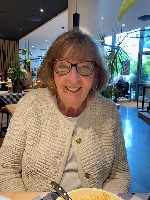 Nancy's older sister wearing cream cardigan and glasses smiling for photo at lunch in a restaurant in Europe