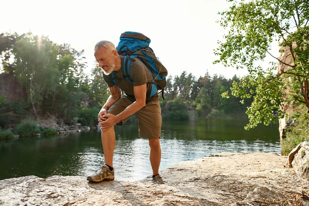 Man hiking in the woods holding his knee in discomfort.