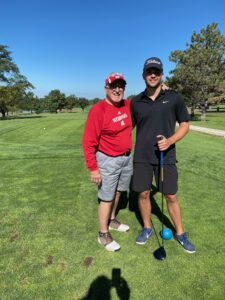 A man and his grandson standing on a golf course and smiling.