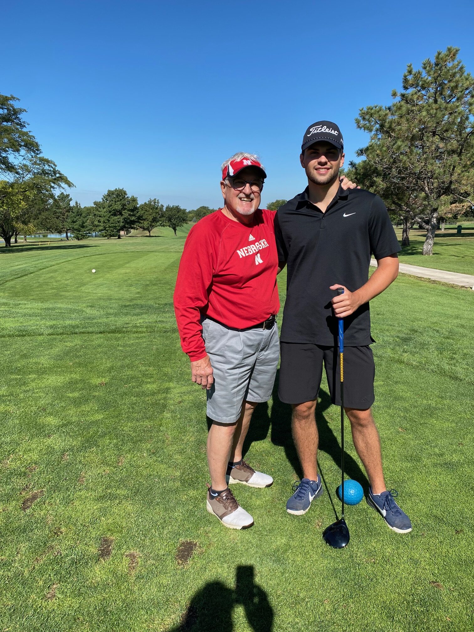 A man and his grandson standing on a golf course and smiling.