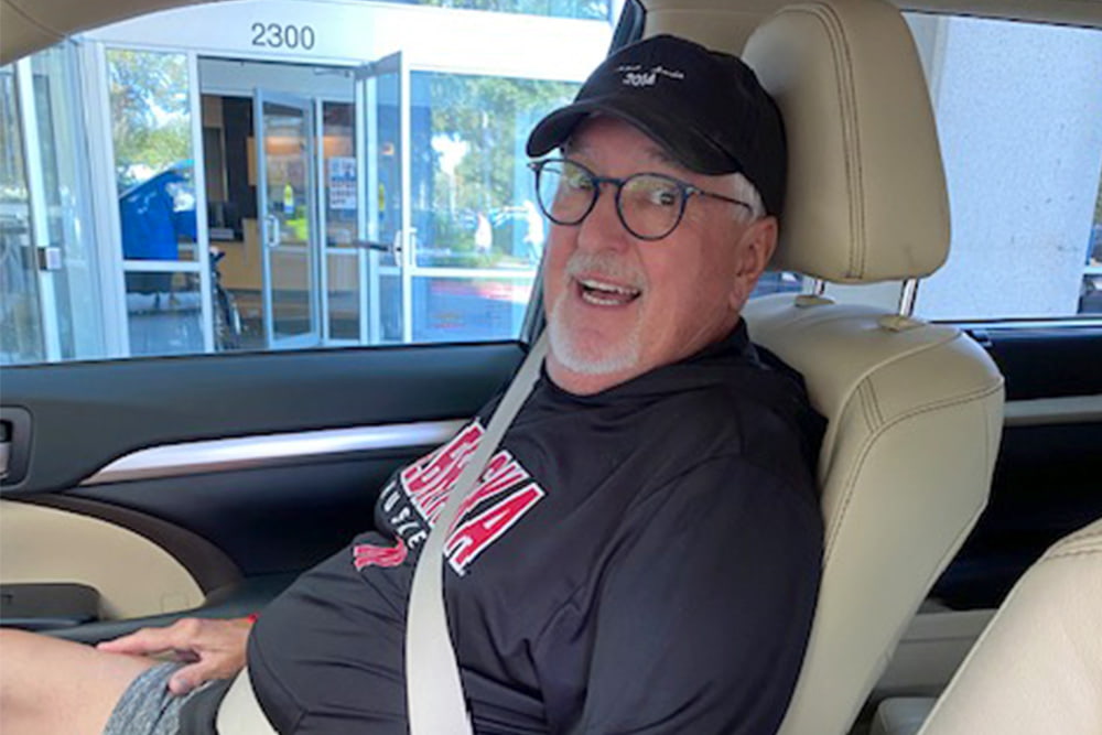 Nancy's husband laughing in the passenger seat of the car.