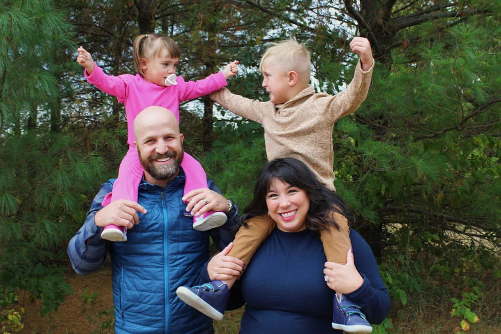 Cassidy and Justin smiling and holding their children on top of their shoulders in nature.