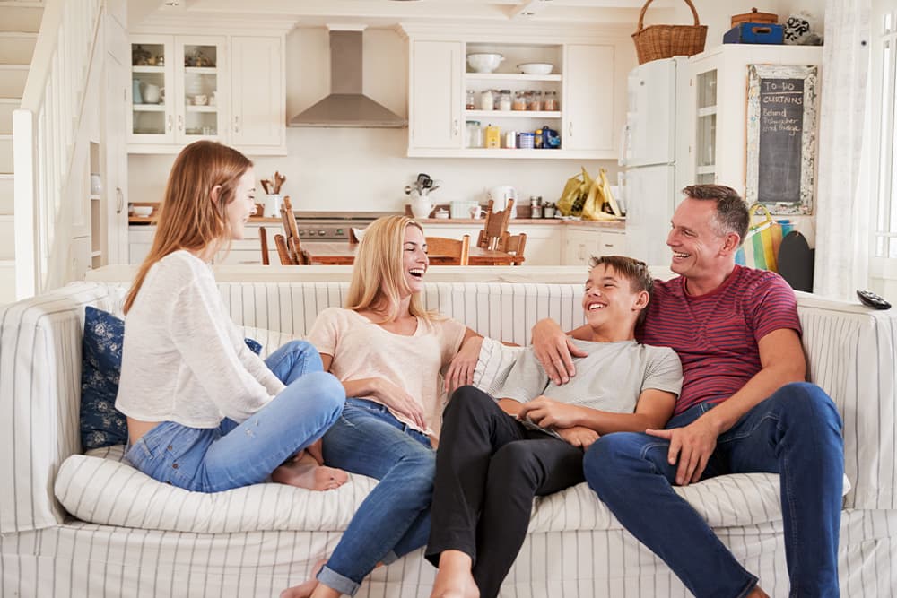 A mom and dad with their son and daughter, all sitting on a couch and laughing together