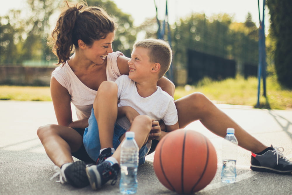 Mother and son sitting on a basketball court smiling at one another