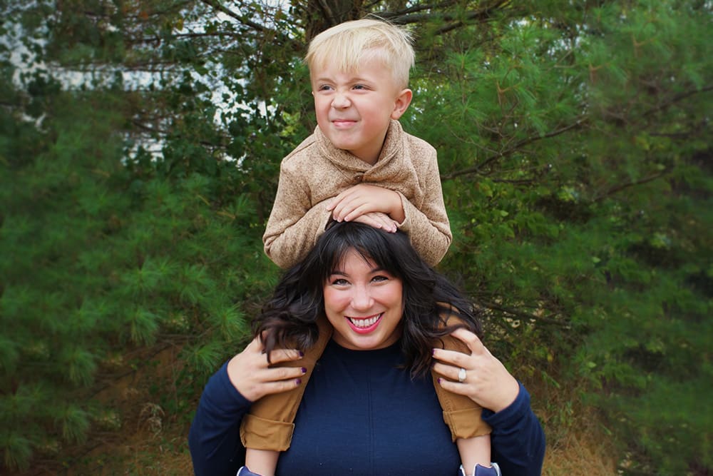 With trees in the background, Cassidy is smiling while holding her son on her shoulders