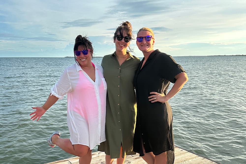 Cassidy and her friends dressed in flowy clothes, smiling with the ocean in the background.