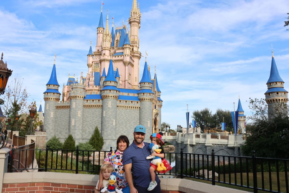 Cassidy, her husband, and their two kids standing in front of Disney castle