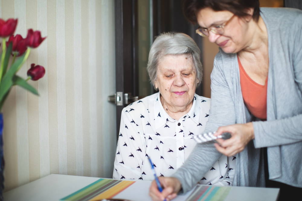 Woman assisting an elderly woman with finding the right medication to take